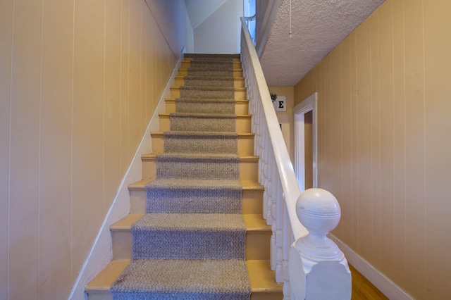 stairs with wooden walls and a textured ceiling