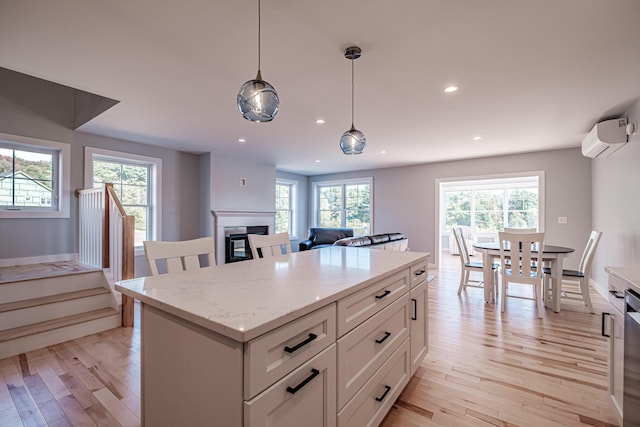 kitchen featuring a wall mounted AC, white cabinets, light stone countertops, pendant lighting, and light hardwood / wood-style flooring