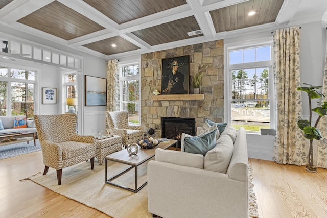 living room featuring light hardwood / wood-style flooring, crown molding, a stone fireplace, and coffered ceiling