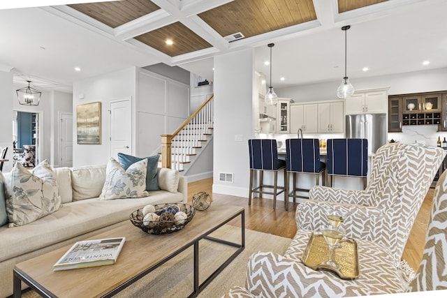 living room with beamed ceiling, crown molding, coffered ceiling, light wood-type flooring, and wood ceiling