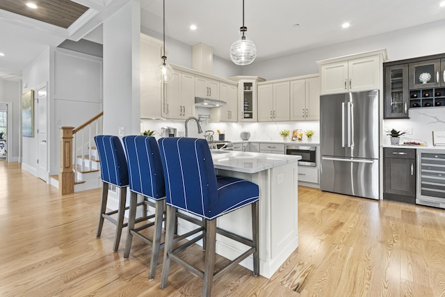 kitchen featuring wine cooler, tasteful backsplash, pendant lighting, light hardwood / wood-style flooring, and appliances with stainless steel finishes