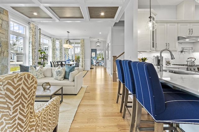 interior space featuring white cabinetry, coffered ceiling, light wood-type flooring, hanging light fixtures, and sink