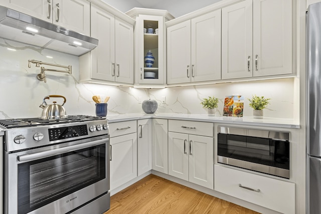 kitchen featuring backsplash, light hardwood / wood-style floors, light stone countertops, appliances with stainless steel finishes, and white cabinets