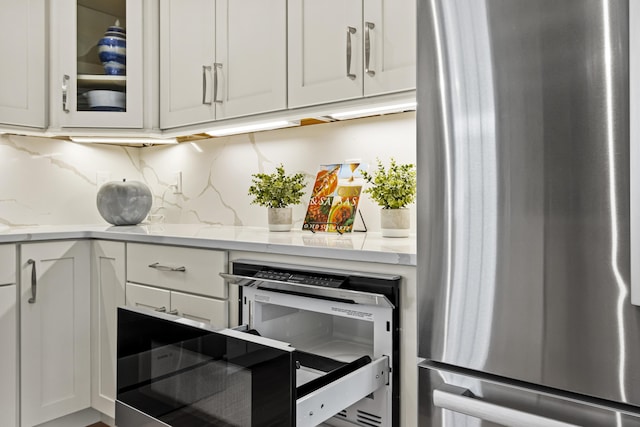 kitchen featuring stainless steel fridge, backsplash, beverage cooler, light stone countertops, and white cabinets