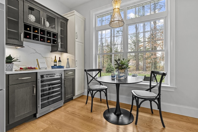 bar with tasteful backsplash, light wood-type flooring, beverage cooler, and pendant lighting