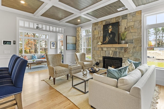 living room with light hardwood / wood-style floors, coffered ceiling, a stone fireplace, crown molding, and beamed ceiling