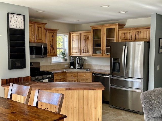 kitchen featuring recessed lighting, stainless steel appliances, butcher block counters, a sink, and glass insert cabinets