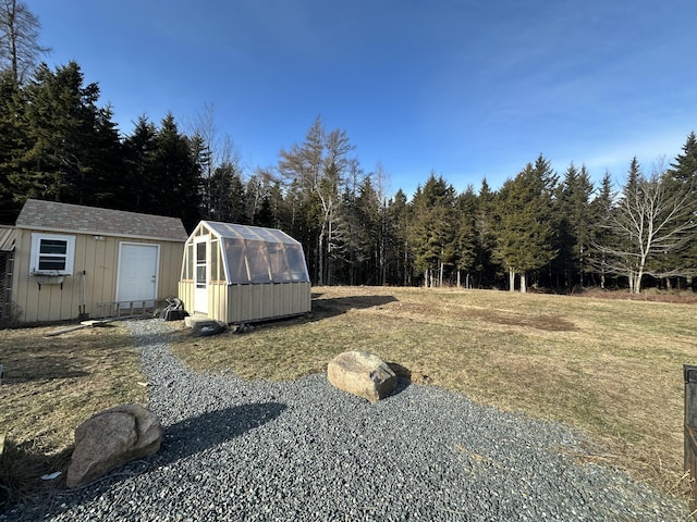 view of yard featuring a forest view, a shed, an exterior structure, and an outdoor structure