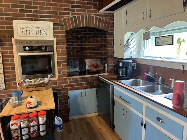 kitchen with brick wall, white cabinets, dishwasher, sink, and oven