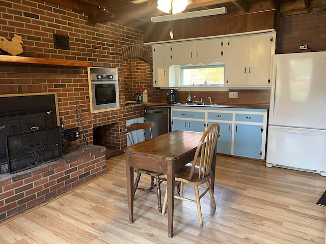 dining space featuring light wood-type flooring, brick wall, sink, and beamed ceiling