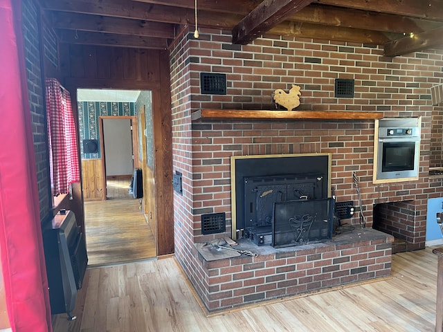 living room featuring beam ceiling, light wood-type flooring, and a wood stove