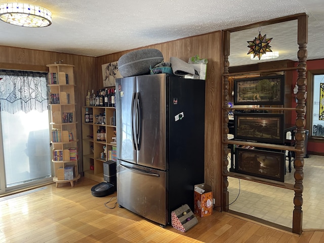 kitchen with a textured ceiling, stainless steel fridge, light wood-type flooring, and wooden walls