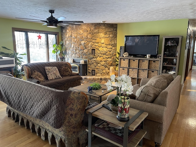 living room with light hardwood / wood-style floors, a textured ceiling, ceiling fan, and a fireplace