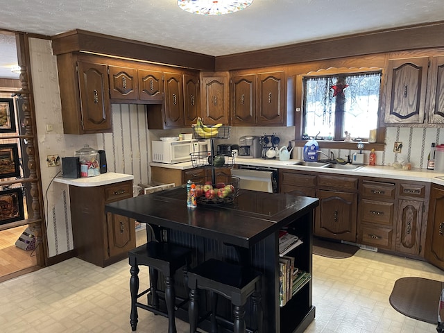 kitchen featuring dishwasher, dark brown cabinets, a textured ceiling, a kitchen island, and sink