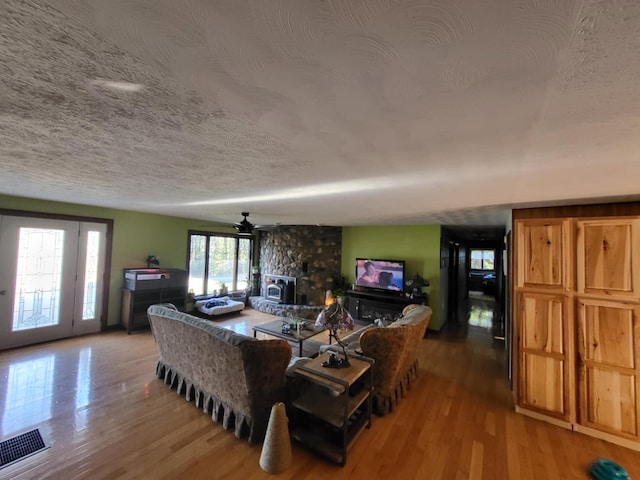 living room featuring ceiling fan, a wood stove, wood-type flooring, and a textured ceiling