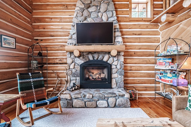 living room featuring wood-type flooring, a stone fireplace, and rustic walls