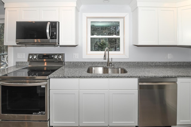 kitchen with white cabinetry, appliances with stainless steel finishes, sink, and dark stone counters