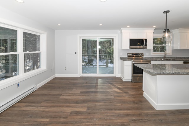 kitchen featuring hanging light fixtures, dark stone countertops, baseboard heating, stainless steel appliances, and white cabinets