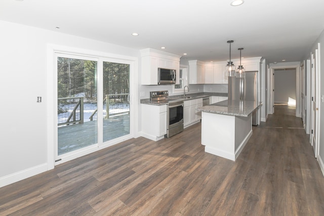 kitchen featuring appliances with stainless steel finishes, white cabinetry, dark stone countertops, hanging light fixtures, and a center island