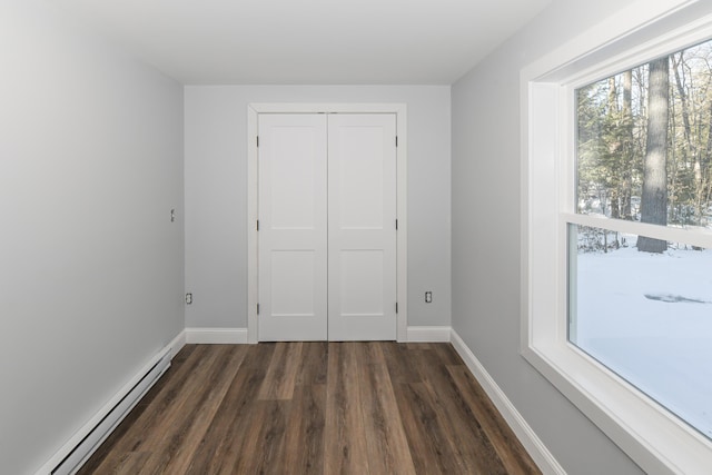 unfurnished bedroom with baseboard heating, dark hardwood / wood-style flooring, and a closet