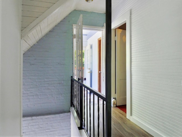 interior space featuring brick wall, lofted ceiling, and wood-type flooring