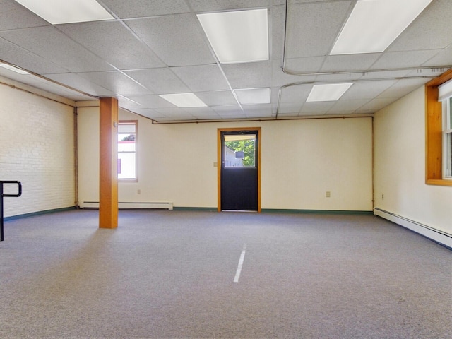 basement featuring brick wall, a baseboard radiator, a wealth of natural light, and a paneled ceiling