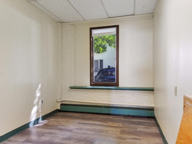 spare room featuring baseboard heating, wood-type flooring, and a paneled ceiling