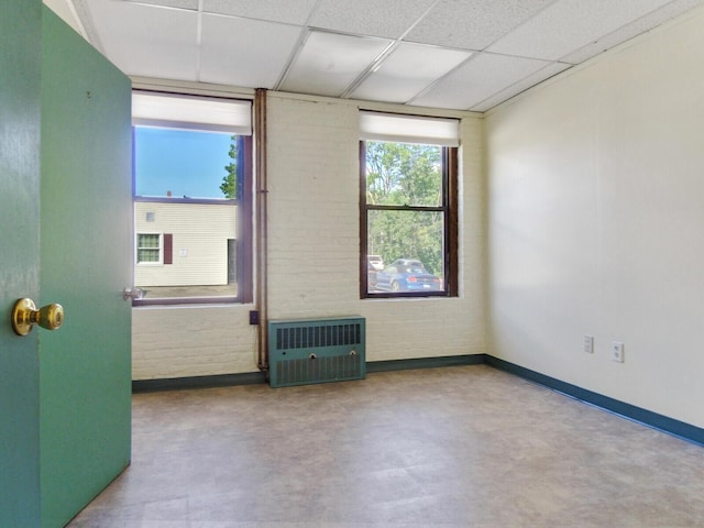 spare room with heating unit, a drop ceiling, and brick wall