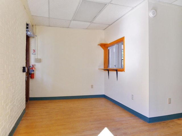 empty room with a paneled ceiling, brick wall, and wood-type flooring