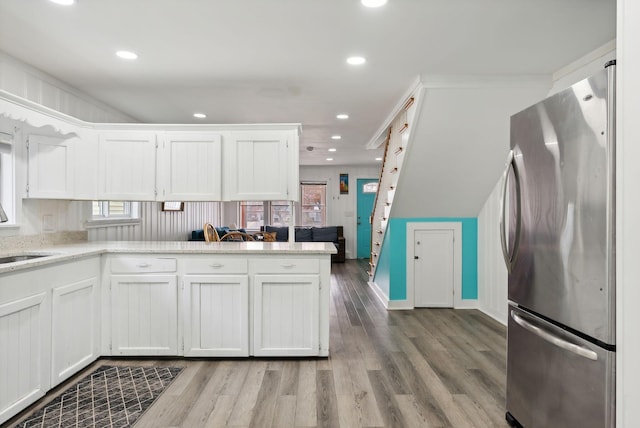 kitchen featuring white cabinets, stainless steel fridge, kitchen peninsula, hardwood / wood-style flooring, and light stone counters