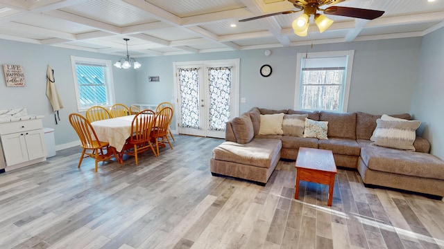 living room featuring ceiling fan with notable chandelier, light hardwood / wood-style floors, french doors, and coffered ceiling