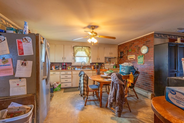 kitchen with ceiling fan, sink, baseboard heating, stainless steel fridge, and brick wall