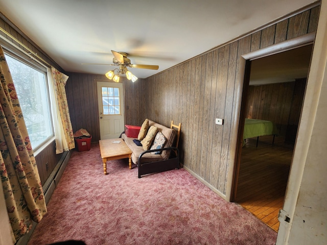 living area with a baseboard heating unit, light colored carpet, ceiling fan, and wood walls