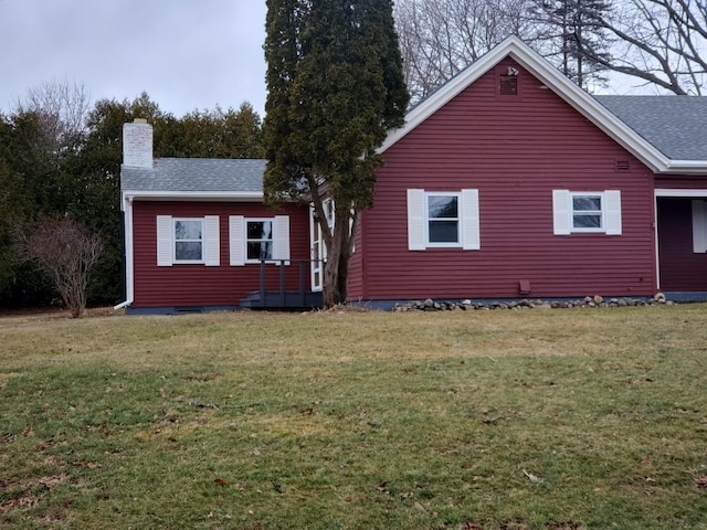 exterior space with roof with shingles, a chimney, and a lawn