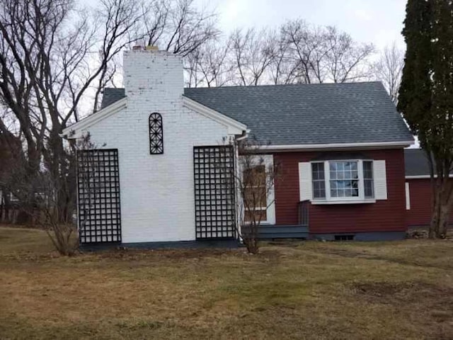 view of front of home with brick siding, roof with shingles, a chimney, and a front yard