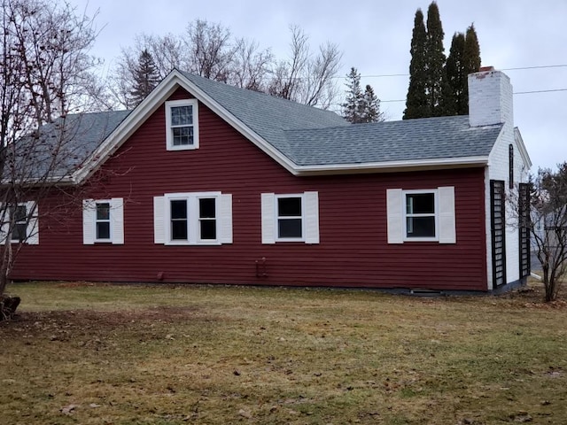 view of side of home with roof with shingles, a chimney, and a yard