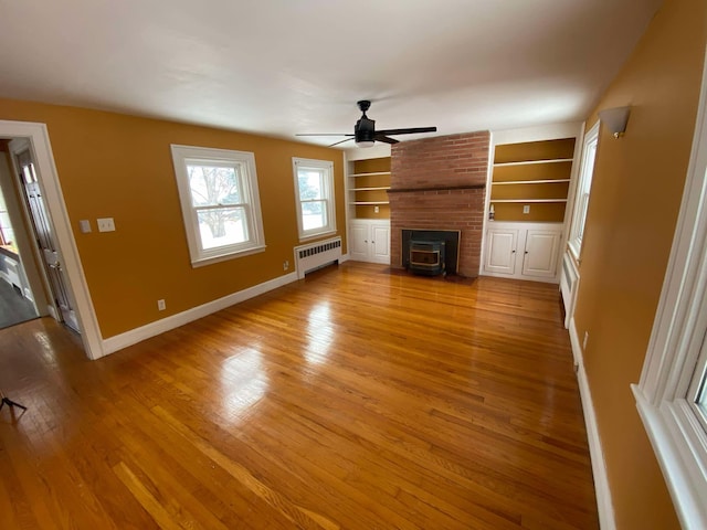 unfurnished living room with built in shelves, light wood-style flooring, a ceiling fan, baseboards, and radiator