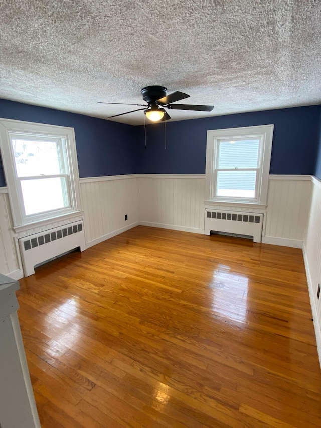 empty room with a wainscoted wall, radiator heating unit, light wood finished floors, and a textured ceiling