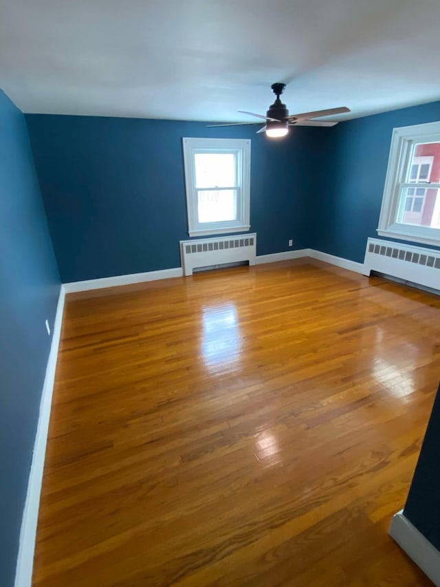 unfurnished room with baseboards, wood finished floors, a ceiling fan, and radiator