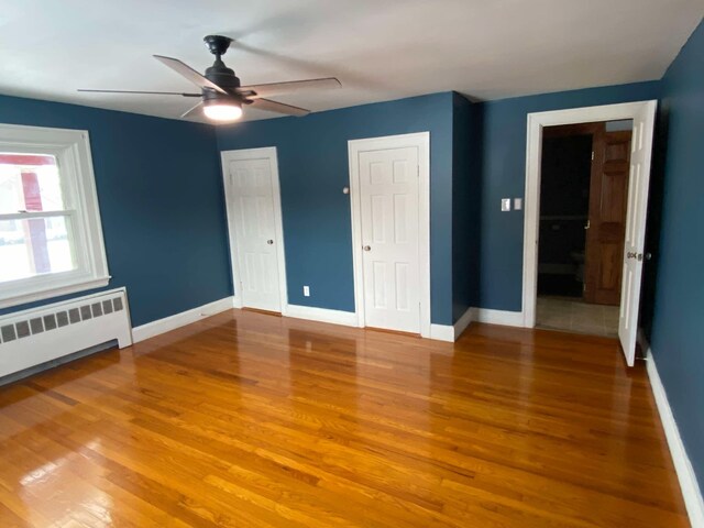 unfurnished bedroom with baseboards, radiator heating unit, and wood finished floors