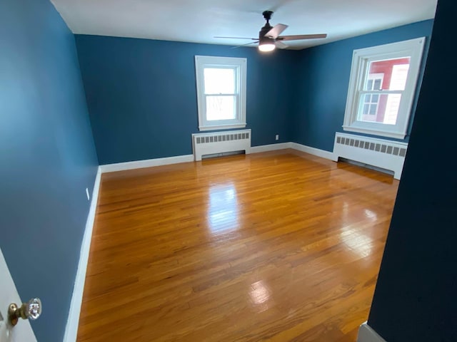 empty room with ceiling fan, radiator heating unit, wood finished floors, and baseboards