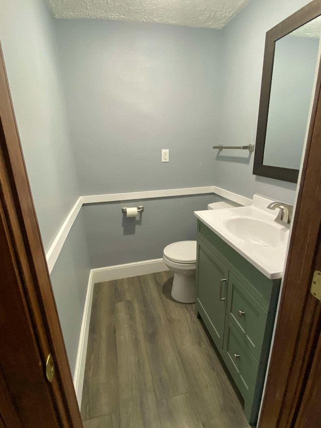 half bathroom featuring a textured ceiling, vanity, wood finished floors, and toilet