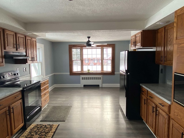 kitchen with radiator, light countertops, electric range, brown cabinetry, and under cabinet range hood