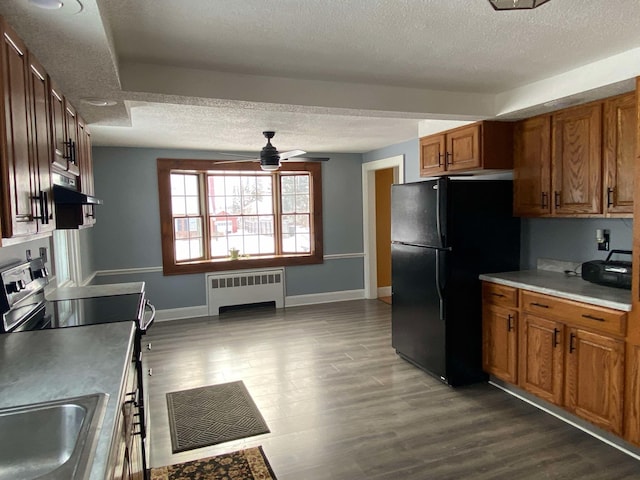 kitchen with brown cabinetry, electric stove, radiator, freestanding refrigerator, and under cabinet range hood