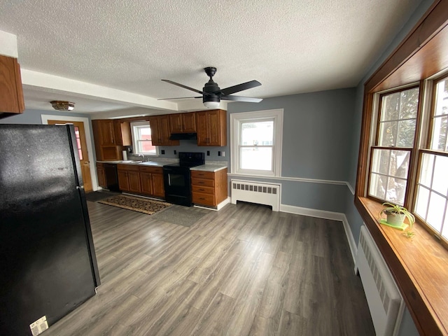 kitchen featuring black appliances, radiator heating unit, light countertops, and brown cabinetry