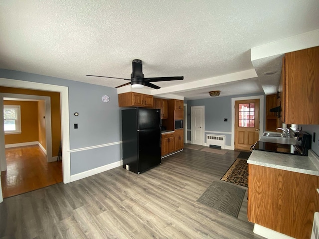 kitchen with light wood finished floors, radiator heating unit, brown cabinets, freestanding refrigerator, and light countertops