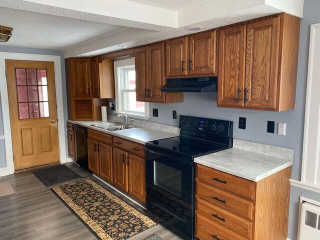 kitchen with under cabinet range hood, a sink, light countertops, brown cabinets, and black appliances