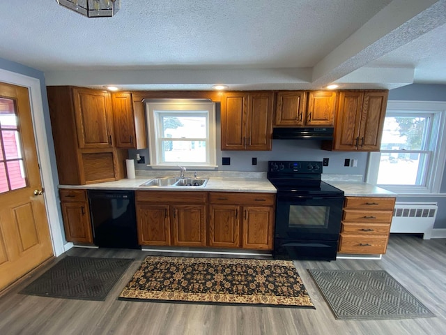 kitchen featuring under cabinet range hood, a sink, light countertops, black appliances, and radiator heating unit