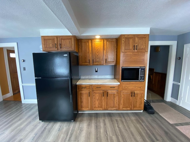 kitchen with brown cabinets, wood finished floors, light countertops, a textured ceiling, and black appliances