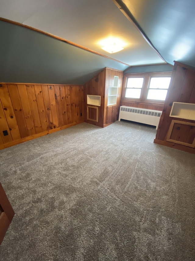 additional living space with lofted ceiling, radiator, wood walls, and dark colored carpet